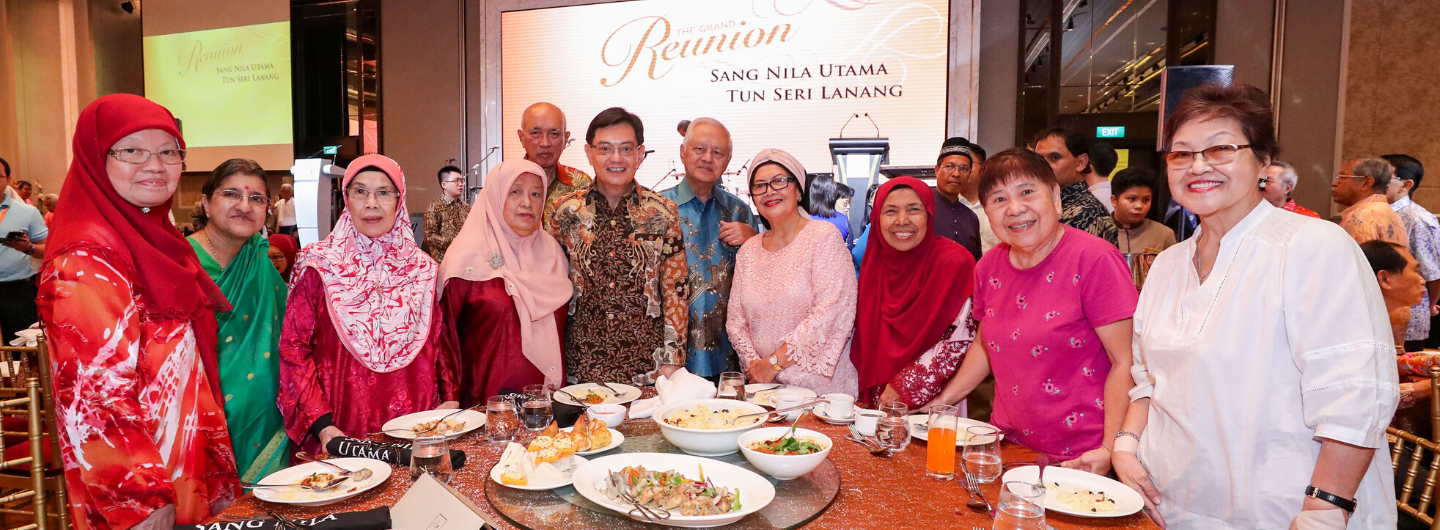 Group of people posing at "The Grand Reunion SANG NILA UTAMA TUN SERI LANANG" event with food on the table.